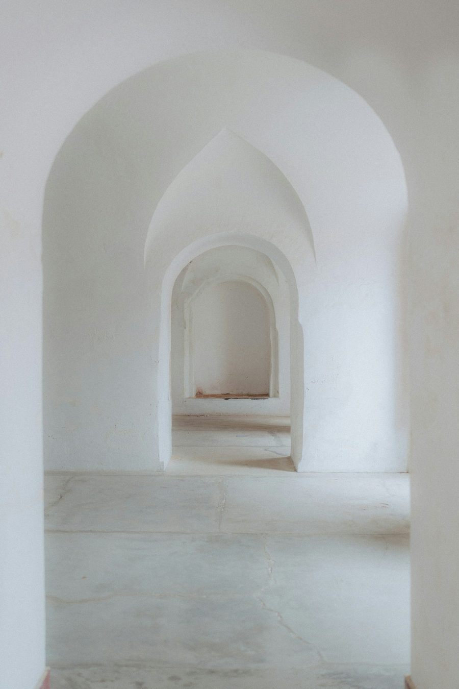 A quiet corridor of pale arched doorways receding into soft daylight.